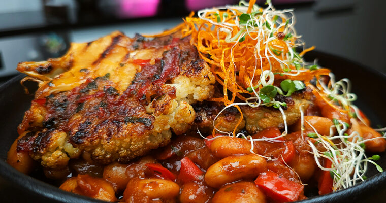 A bowl of roasted cauliflower served with butter beans and vegetables in a miso sauce, garnished with fresh thyme.