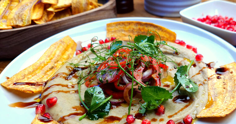 A fine dining plate of creamy green plantain and parsnip purée topped with crispy plantain chips, micro herbs, and pomegranate.